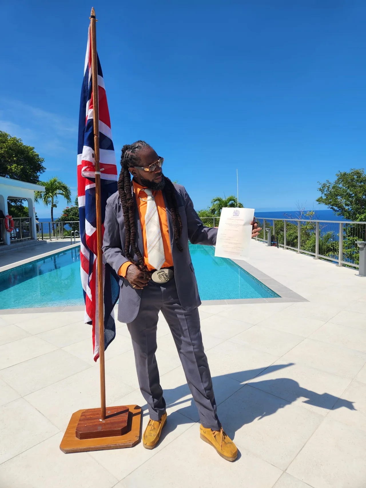Vere Hendrickson holding his citizenship certificate beside the Union flag in Montserrat.