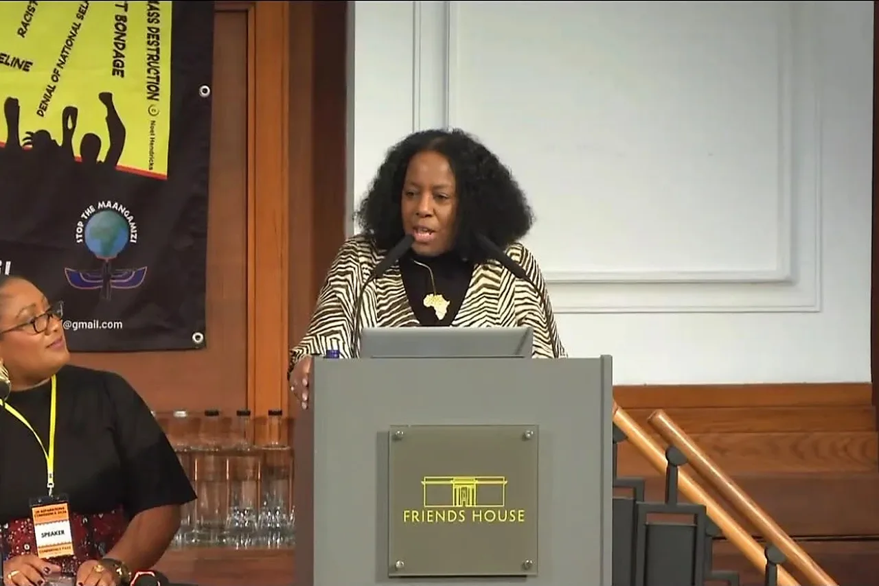 Jacqui McKenzie, in a zebra-print jacket, speaking at a podium marked Friends House.