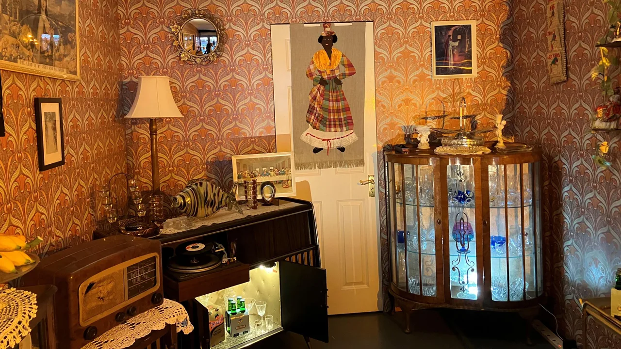 The Dominican Front Room display, with patterned wallpaper, a glass cabinet, record player and wooden radio.